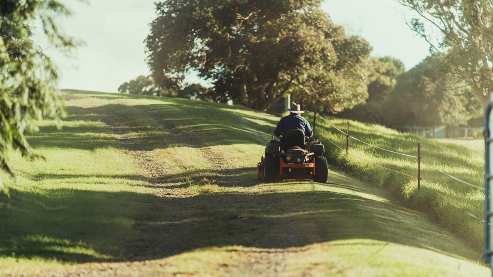 Man riding a red and black ATV on a green field, on a sunny day