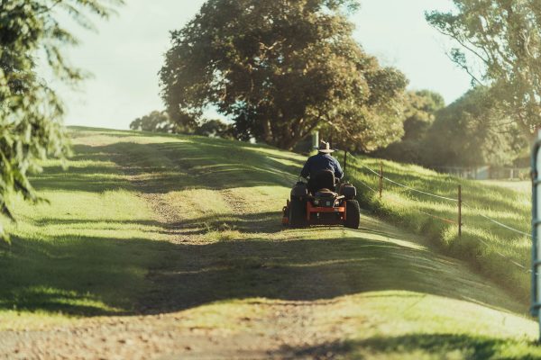 Man riding a red and black ATV on a green grass field, on a sunny day